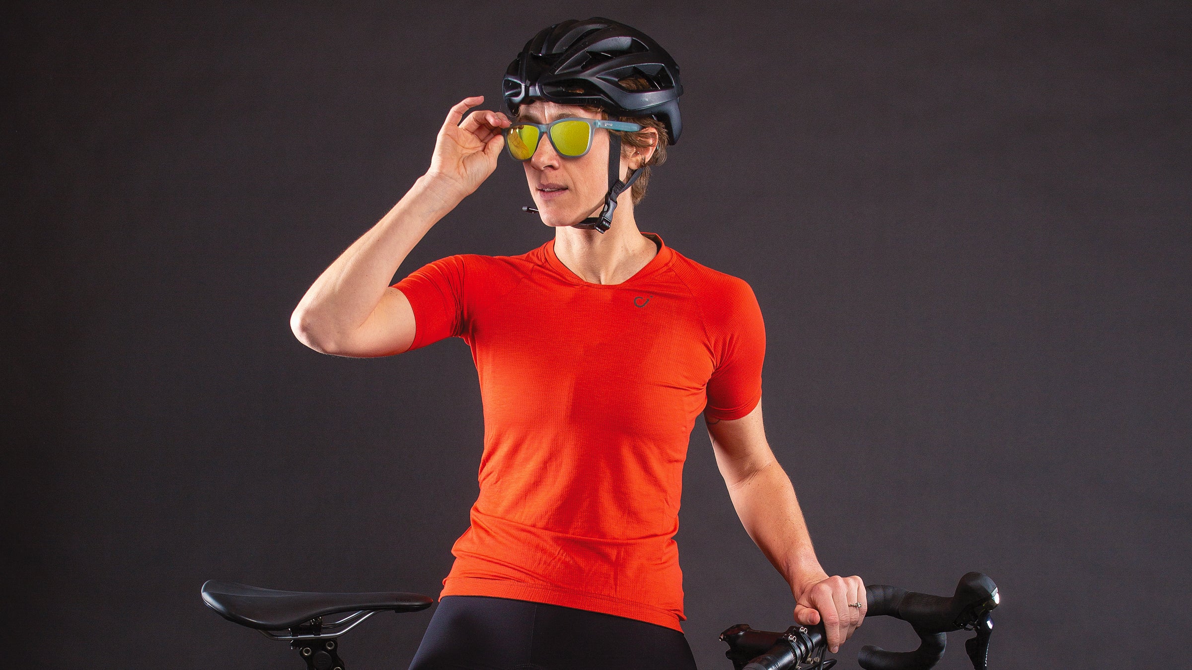Woman in gravel cycling gear leans on a gravel bike and adjusts her sunglasses