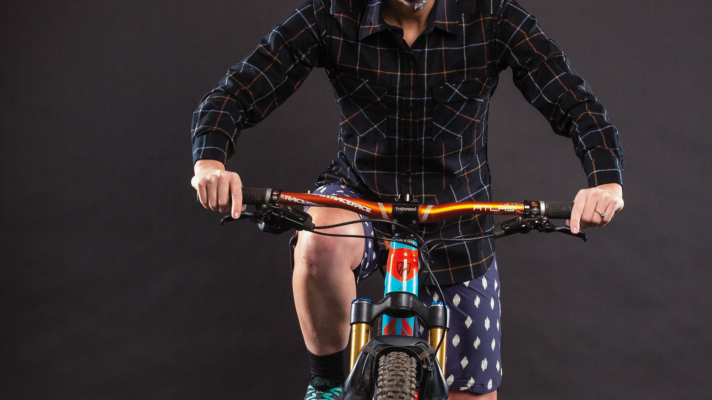 Detail of woman sitting on mountain bike wearing button-up shirt and shorts