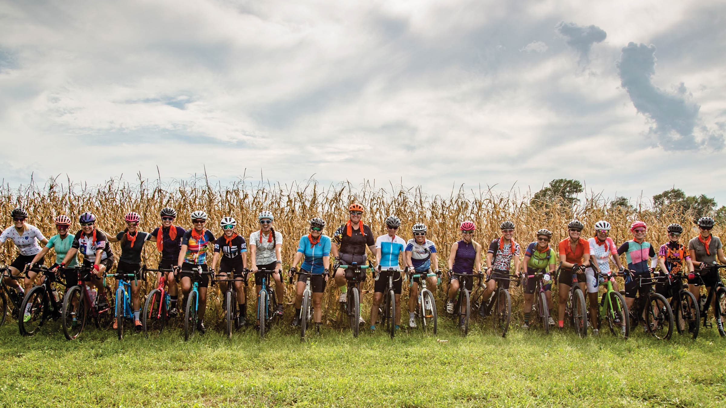 Women on gravel bikes line up in front of a corn field