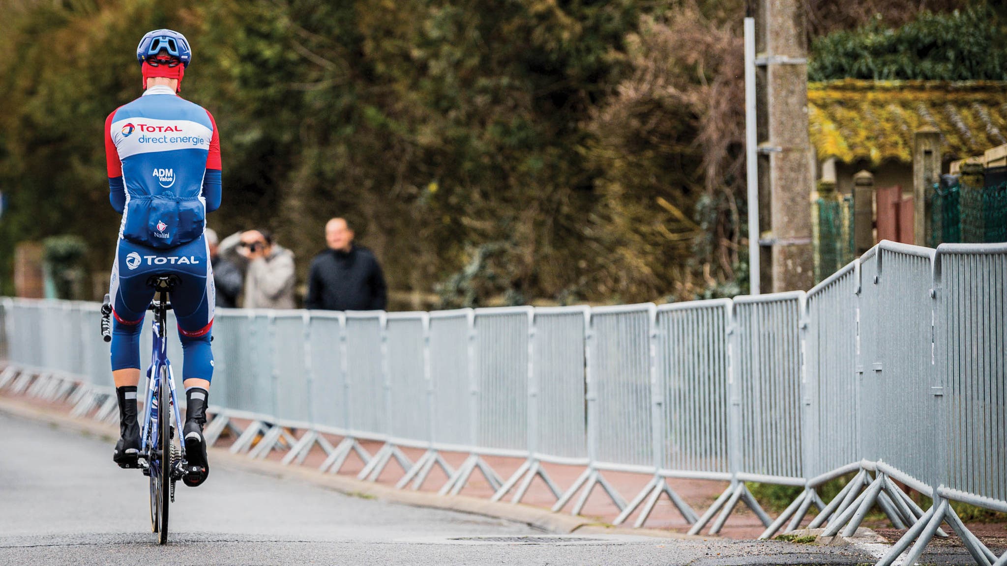 Single cyclist sitting up with back to the camera with metal fencing lining the road