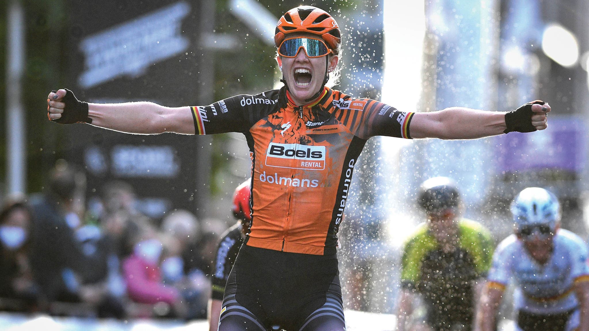 Woman in orange jersey sits up to celebrate crossing the finish